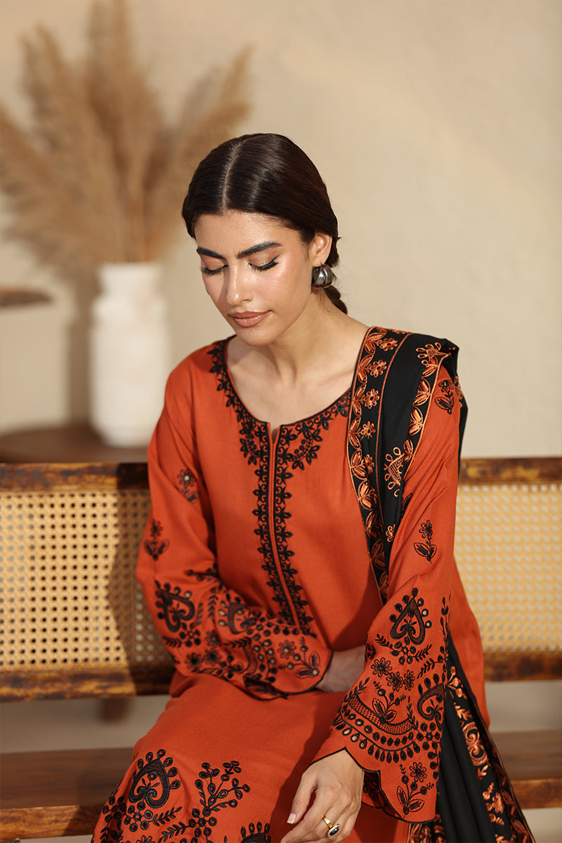 Woman wearing an orange and black embroidered traditional outfit sitting indoors.