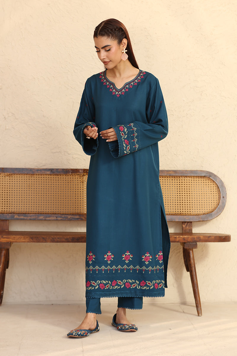 Woman wearing a blue embroidered outfit standing in front of a wooden bench.