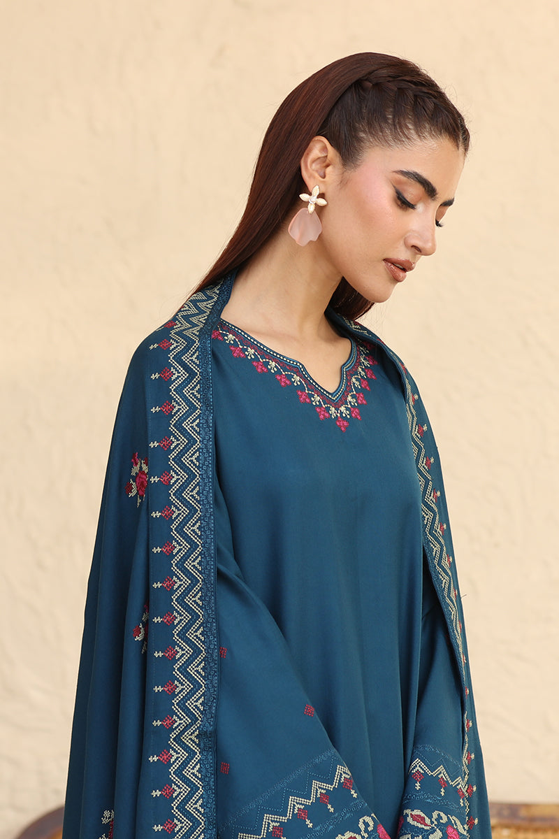 Woman wearing a teal outfit with intricate patterns on a beige background