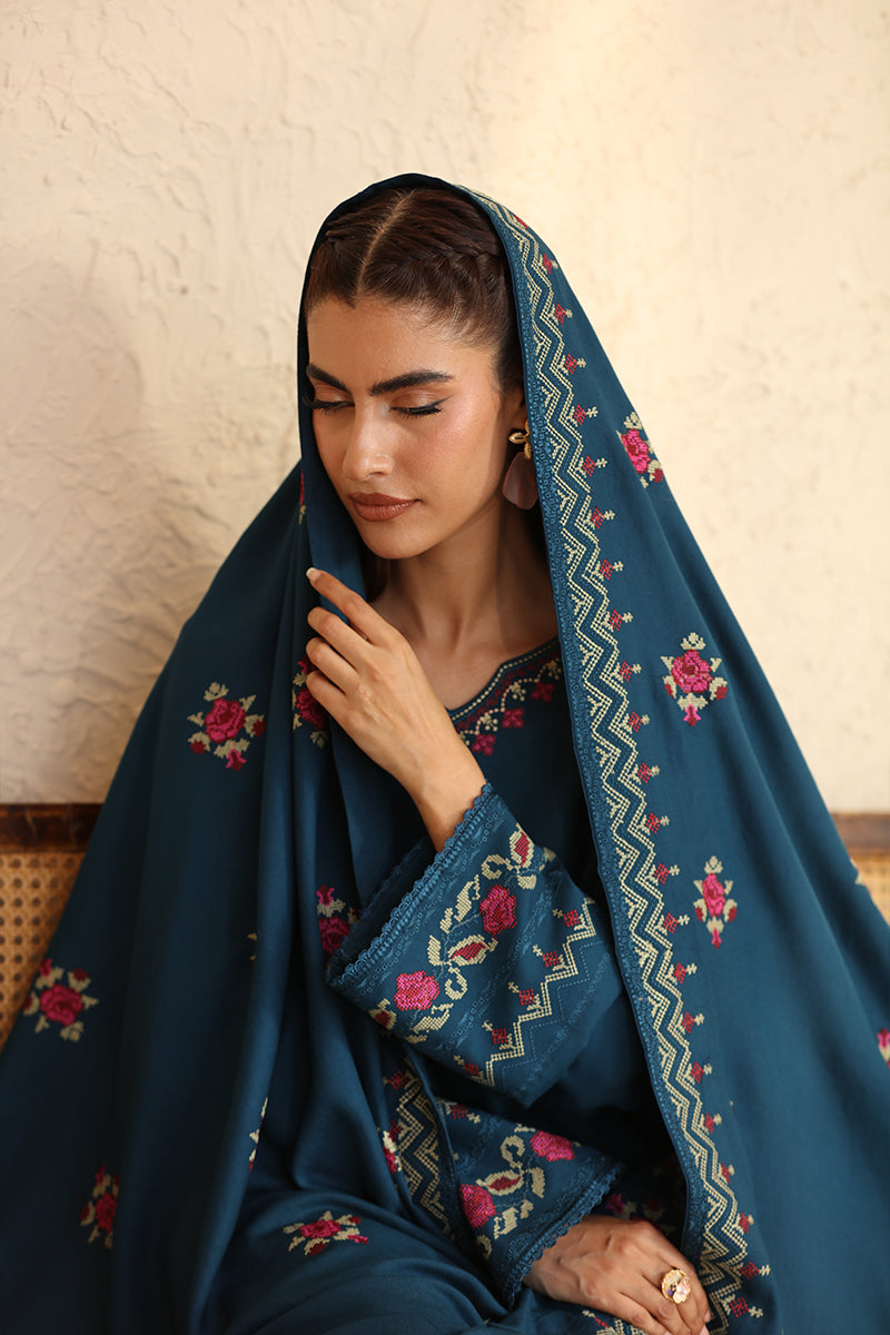 Woman wearing a blue embroidered headscarf with a neutral background
