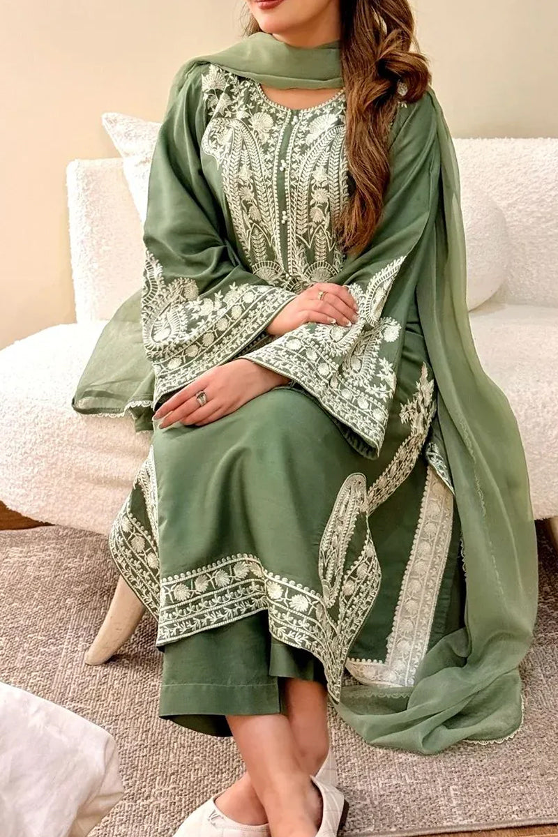 Woman wearing a green embroidered traditional outfit sitting on a white couch.