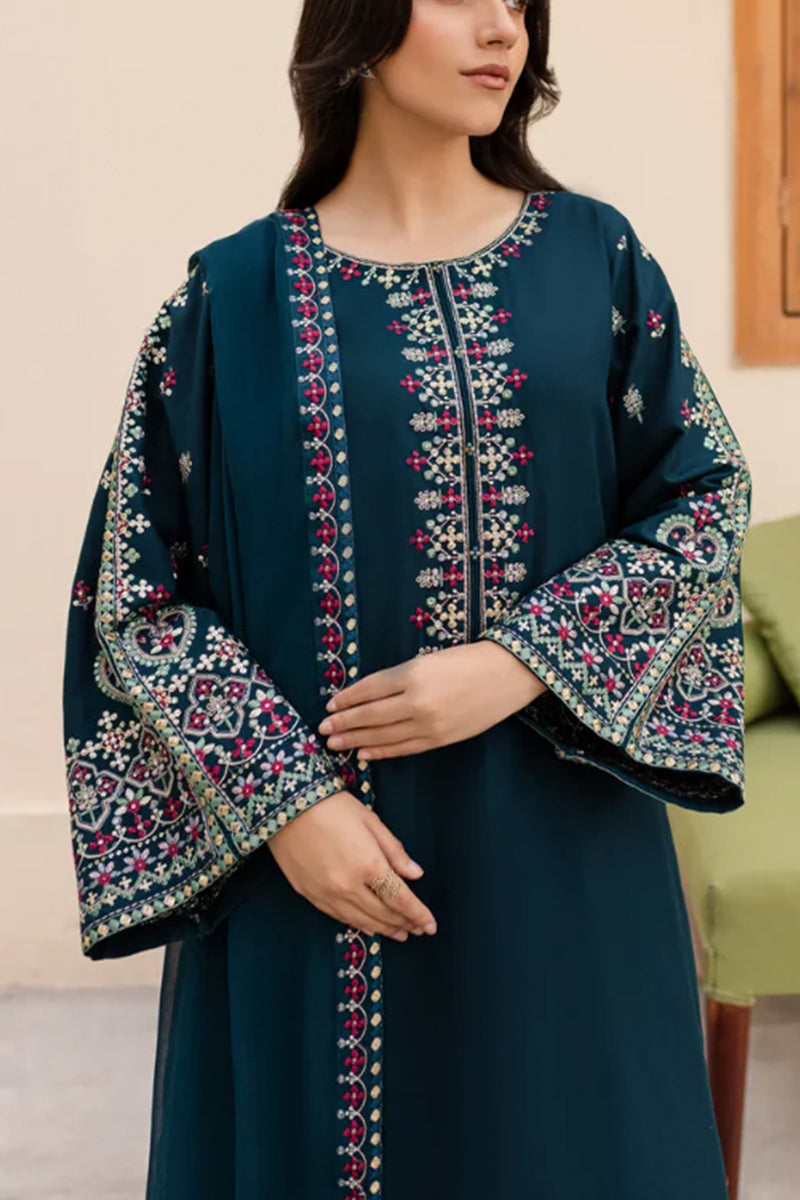 Woman wearing a dark blue dress with intricate embroidery in a room.