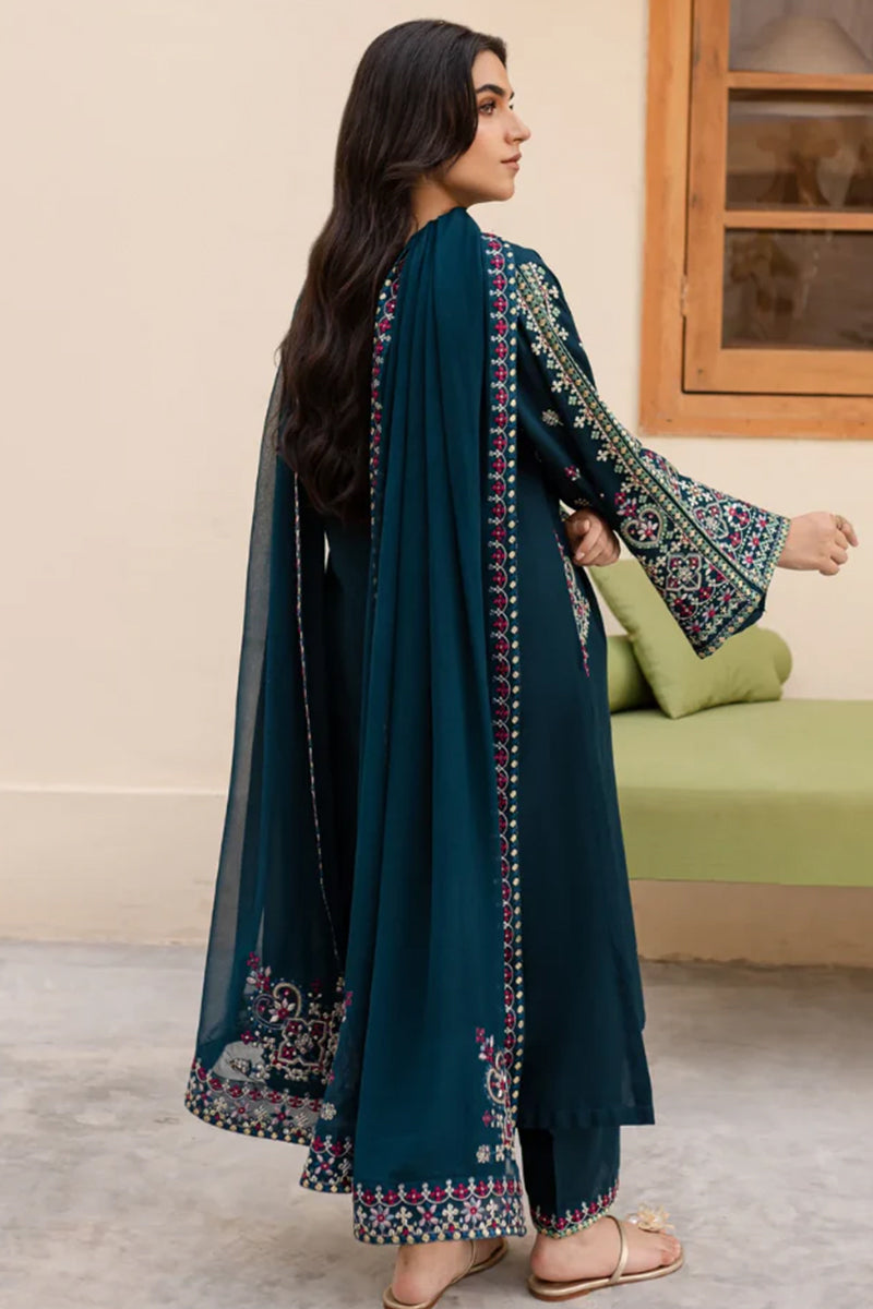 Woman wearing a teal embroidered outfit in a room with a green sofa.