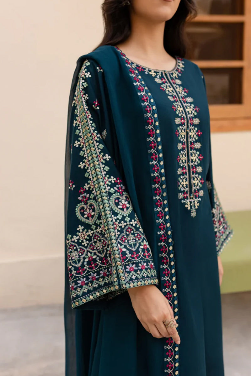 Woman wearing a dark green embroidered traditional outfit indoors.