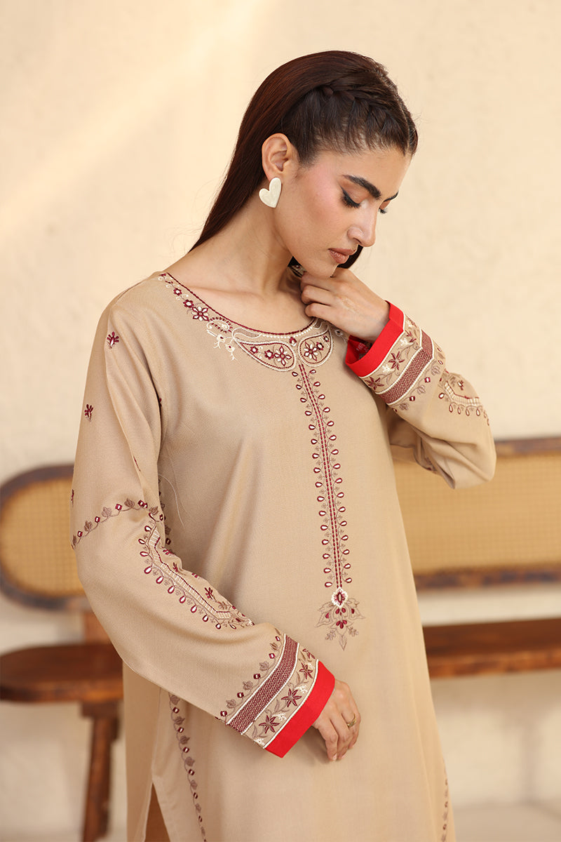 Woman wearing a beige embroidered dress with red details in an indoor setting.