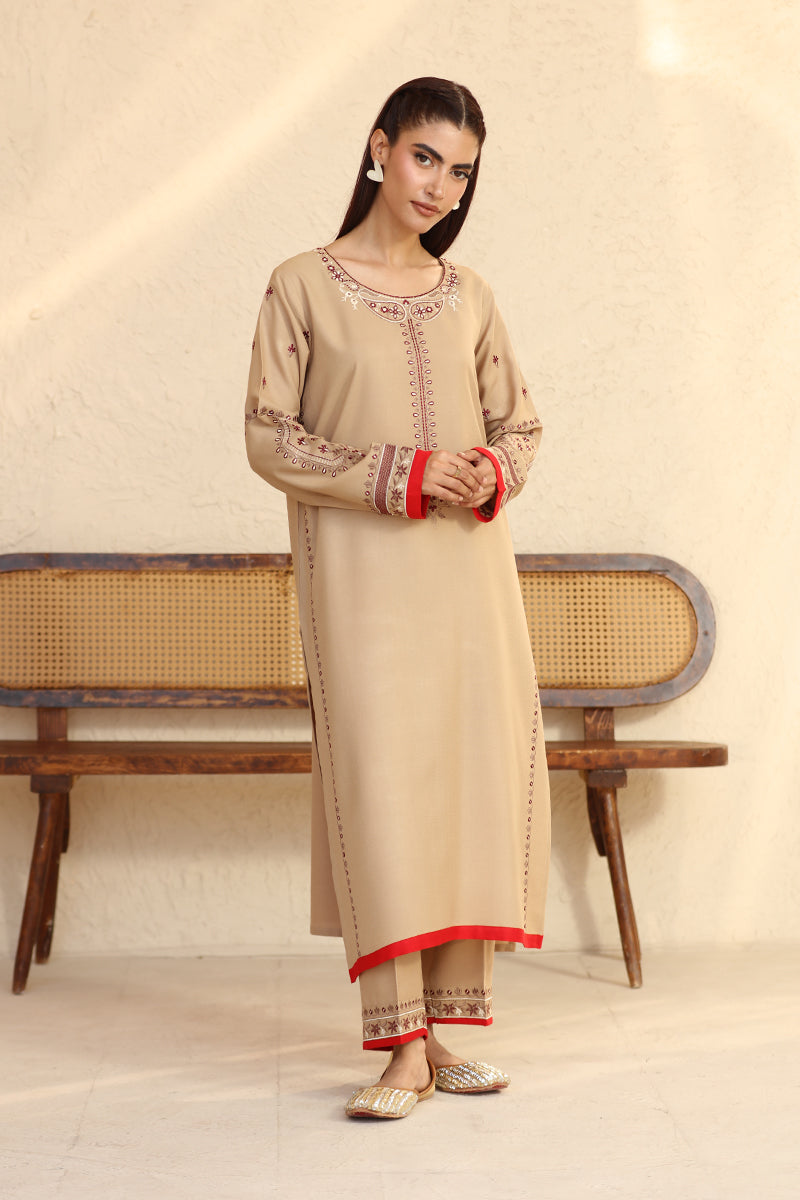 Woman wearing a beige traditional outfit with red accents in a minimalistic setting.