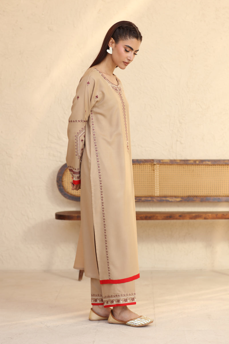 Woman wearing a beige traditional outfit with red accents in a minimalistic setting.