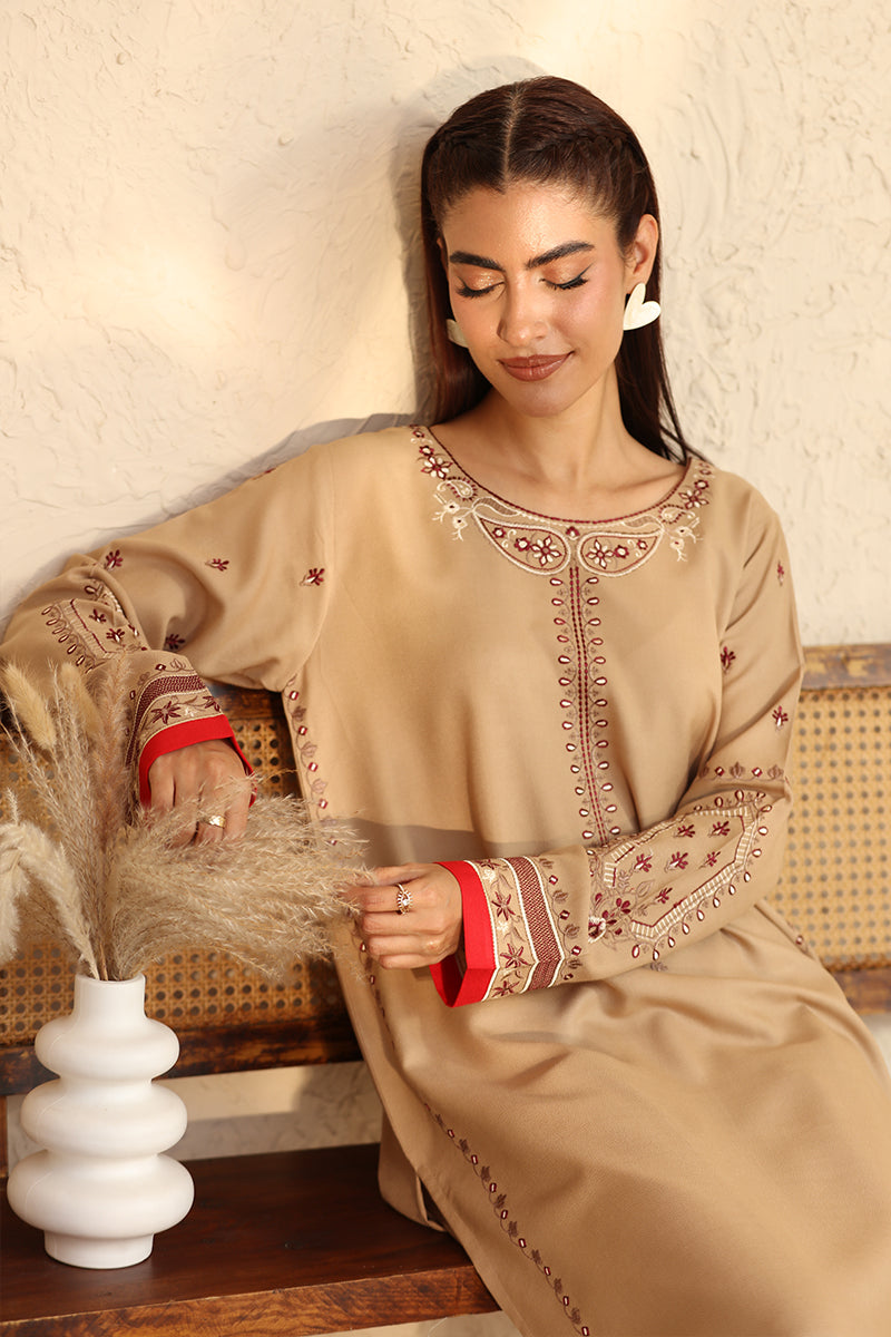 Woman wearing a beige embroidered dress sitting on a wooden bench.
