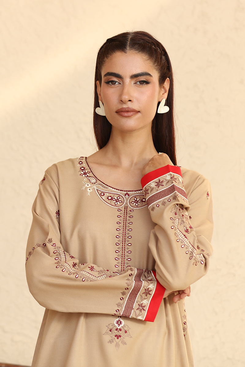 Woman wearing a beige embroidered dress with a red accent on a beige background