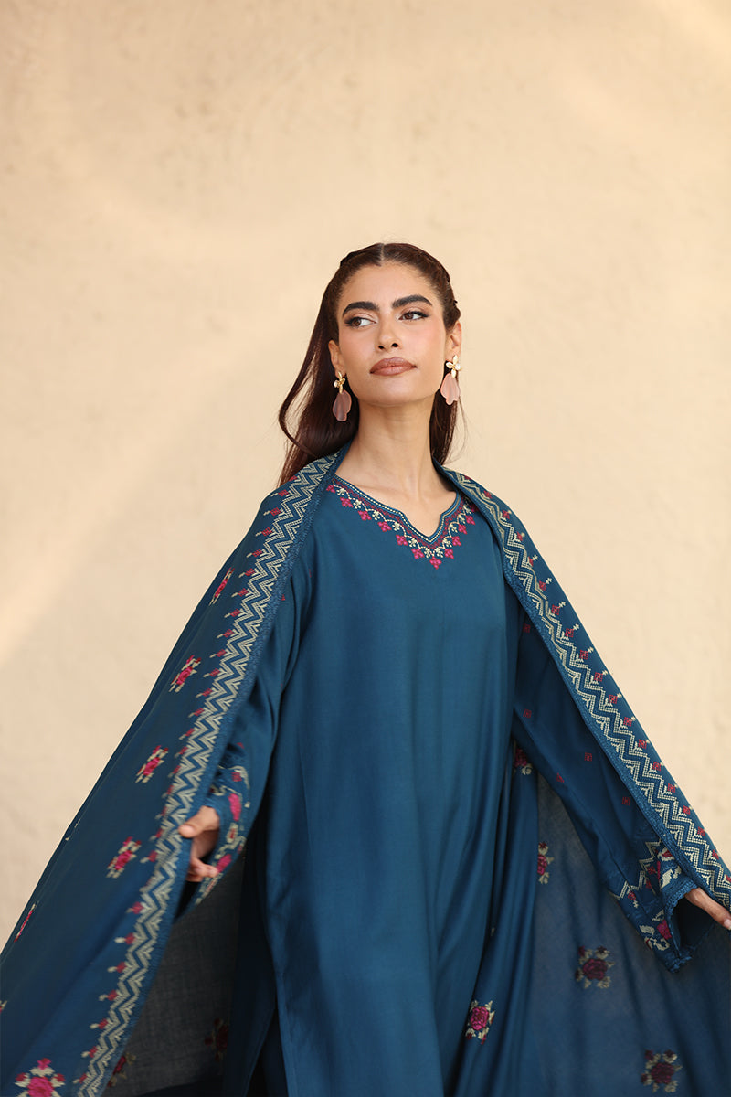 Woman wearing a blue traditional outfit with embroidered sleeves against a beige background