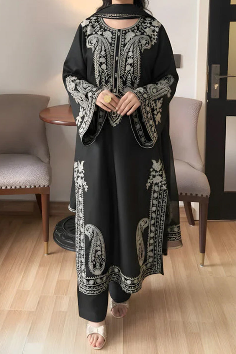 Person wearing a black and white embroidered outfit in a room with chairs and a table.