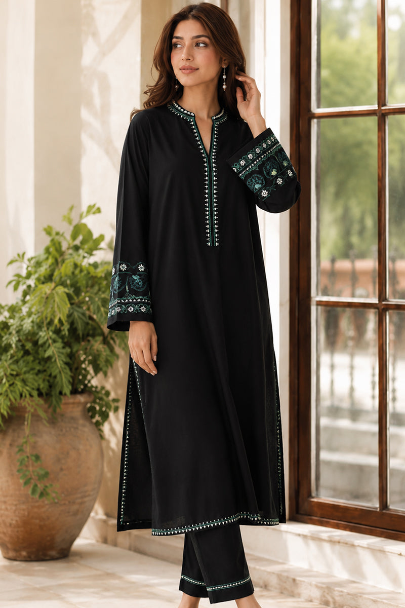 Woman wearing a black outfit with green embroidery indoors.
