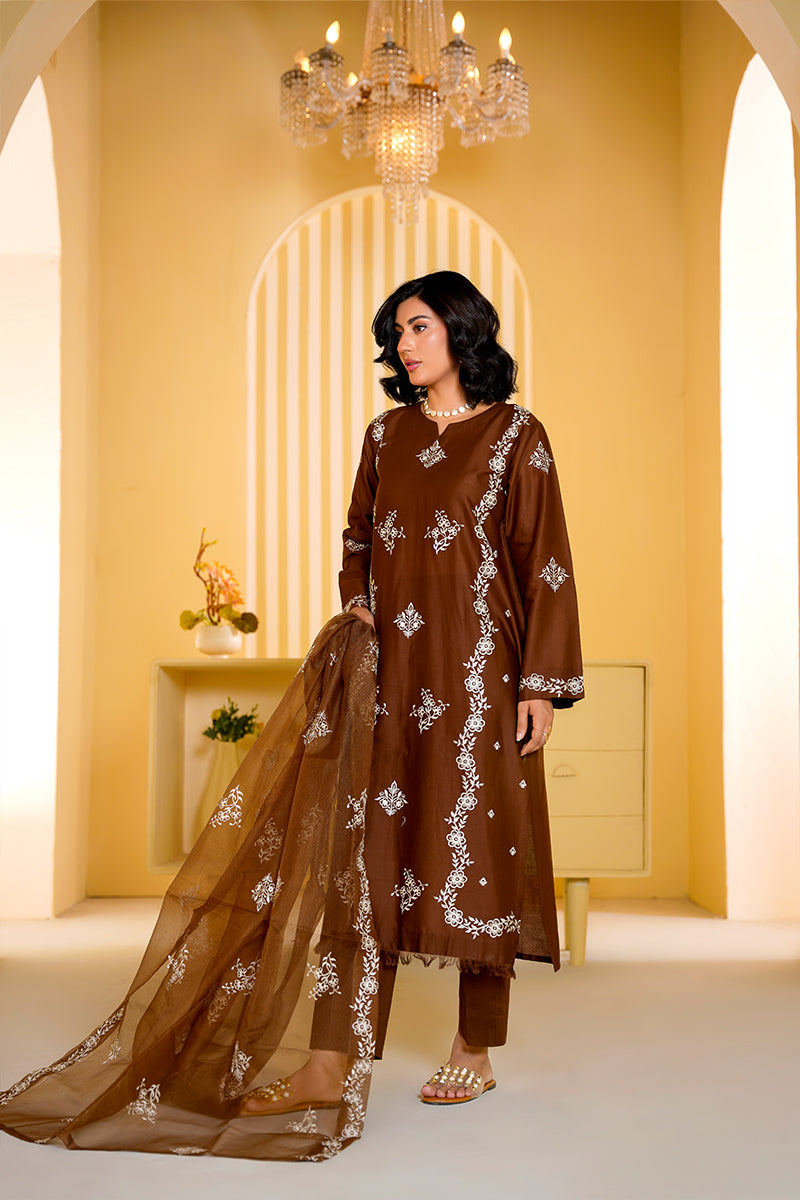 Woman in a brown embroidered outfit standing in a well-lit room with a chandelier.