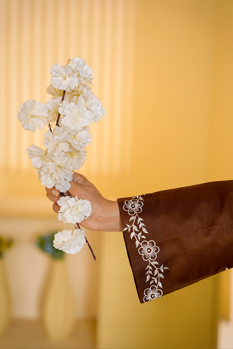 Hand holding a branch of white flowers against a yellow background