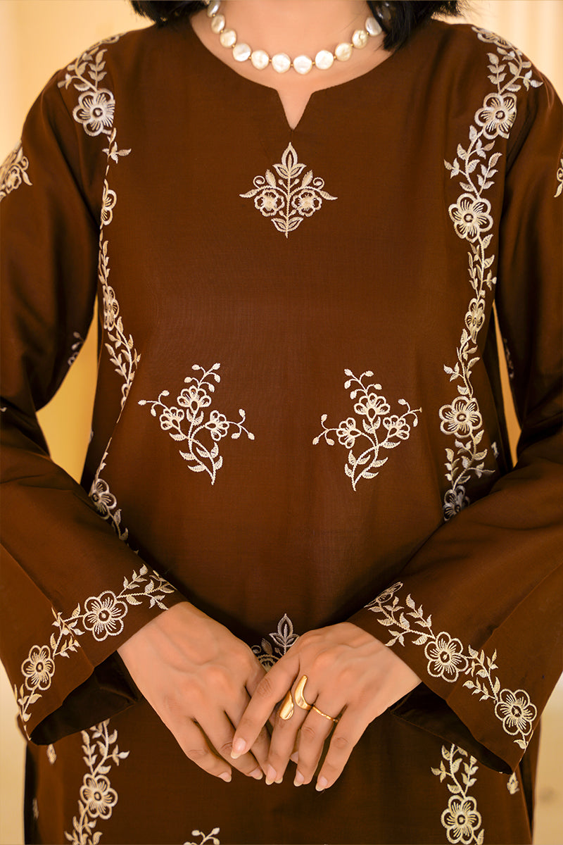 Brown traditional outfit with white floral embroidery on a beige background