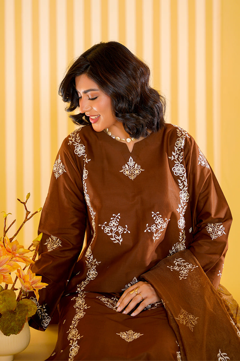 Woman wearing a brown traditional outfit with white patterns against a yellow curtain background