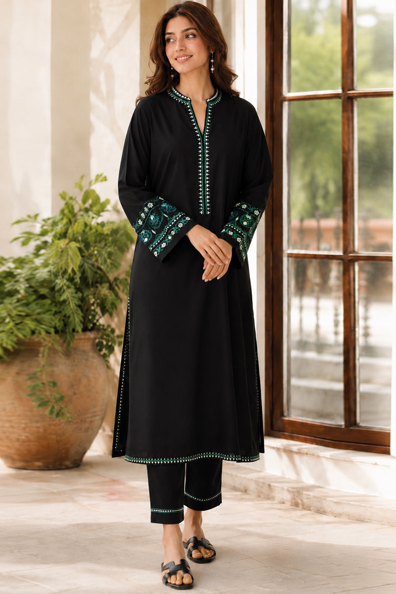 Woman wearing a black kurta with green embroidery in a bright room.