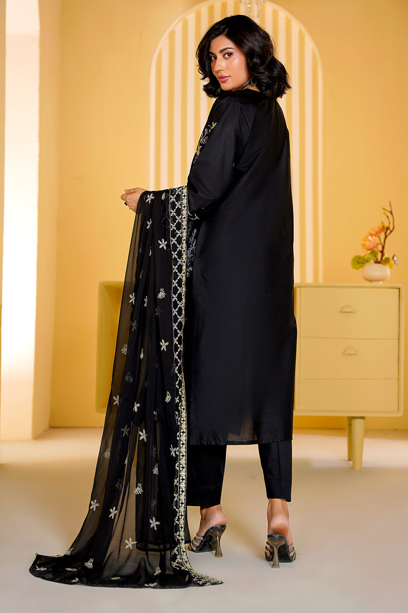 Woman in a black outfit holding a black dupatta with white patterns in a bright room.