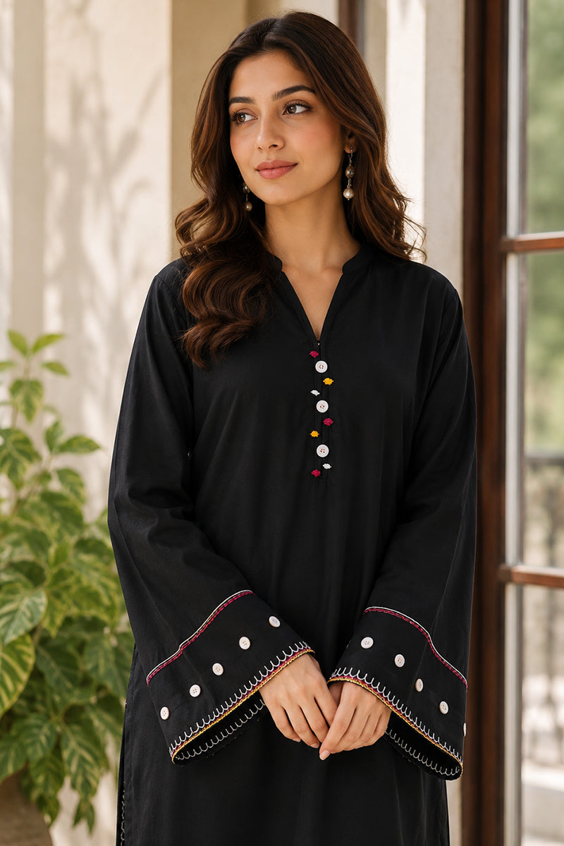 Woman wearing a black outfit with decorative cuffs and buttons, standing indoors.