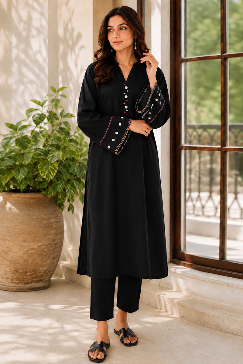 Woman in a black outfit standing indoors with a plant and window in the background