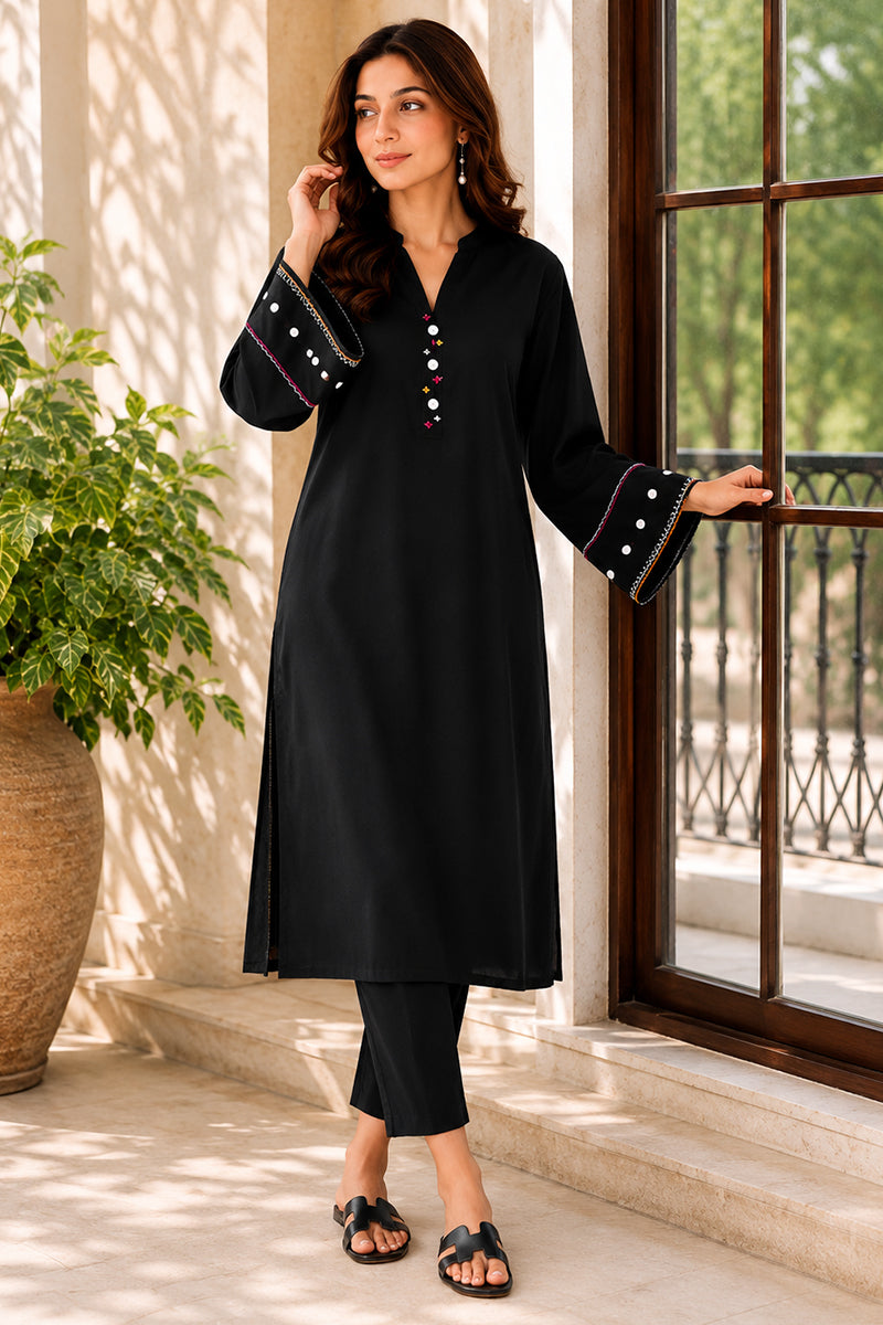 Woman wearing a black kurta with white embroidery standing by a window.
