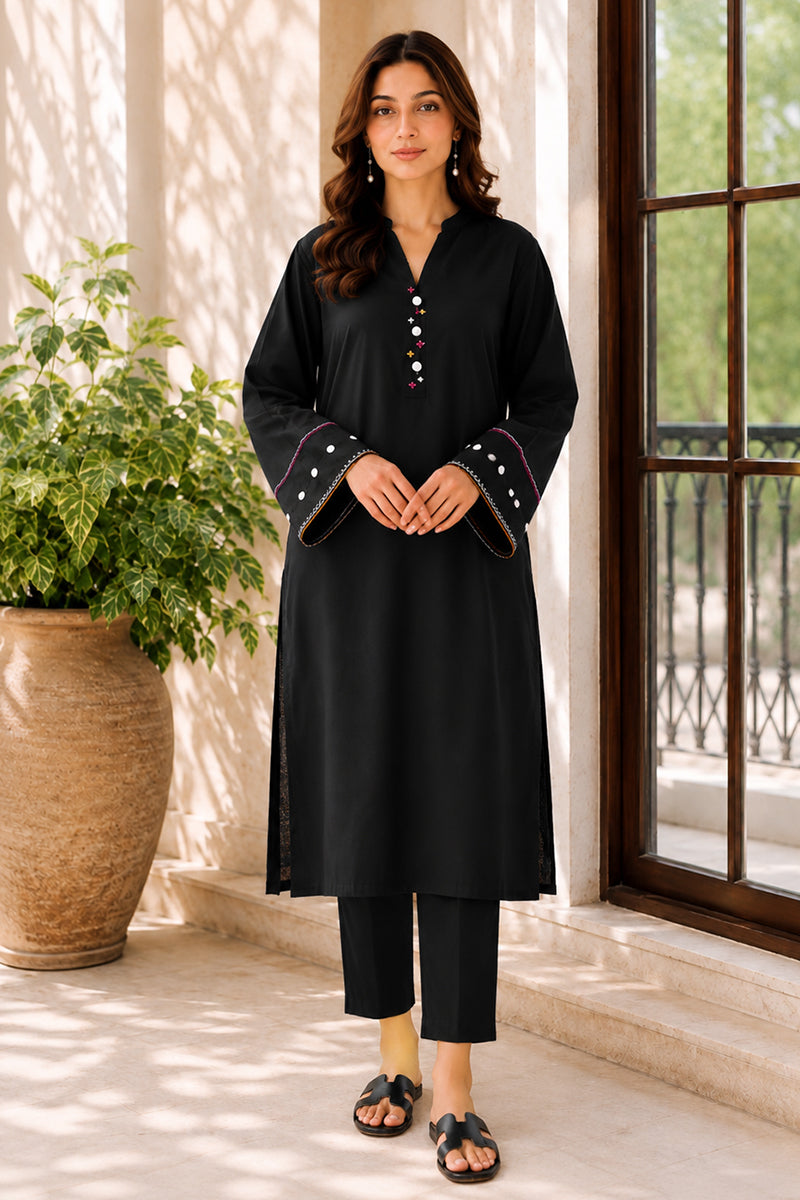 Woman wearing a black outfit with decorative elements standing in a sunlit room.